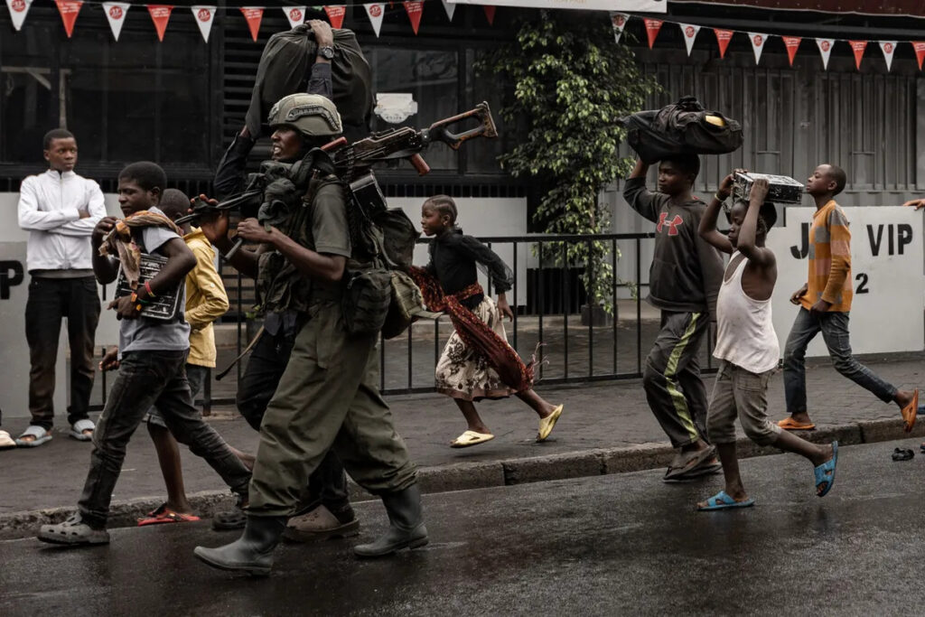 © STR / AFP Un membre du groupe armé M23 marche aux côtés des habitants dans une rue du quartier de Keshero à Goma (RDC), le 27 janvier 2025.